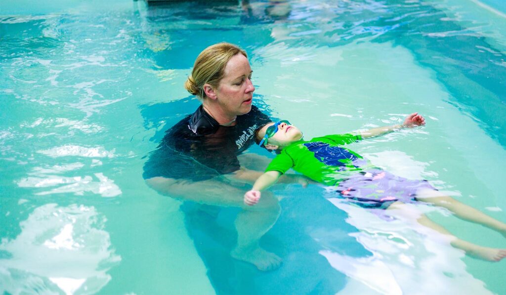 Trainer helping child floating on back